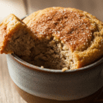 একটি মাগে তৈরি নরম, সোনালি-বাদামী কলার কেক, যার উপরিভাগে দারচিনি বা চিনির গুঁড়ো ছিটানো।