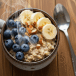 একটি সিরামিকের মাগে তাজা কলা, ব্লুবেরি এবং বাদাম দিয়ে সাজানো গরম ওটমিল।