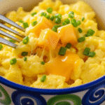 একটি রঙিন সিরামিকের মাগে তুলতুলে ভাজা ডিম, উপরে চিবানো চাইভস এবং গলানো পনির।